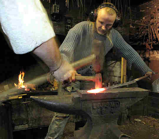 A smith using a striker and assistant on the sledge hammer